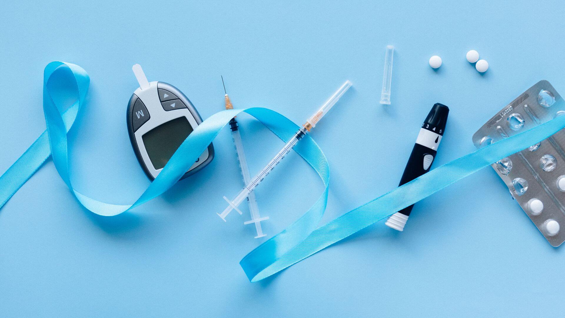 Diabetes management supplies, including a glucometer, insulin syringes, a pen, pills, and a blue ribbon, are arranged on a light blue background, perfect for those looking to buy diabetic test strips or manage unused test strips responsibly.